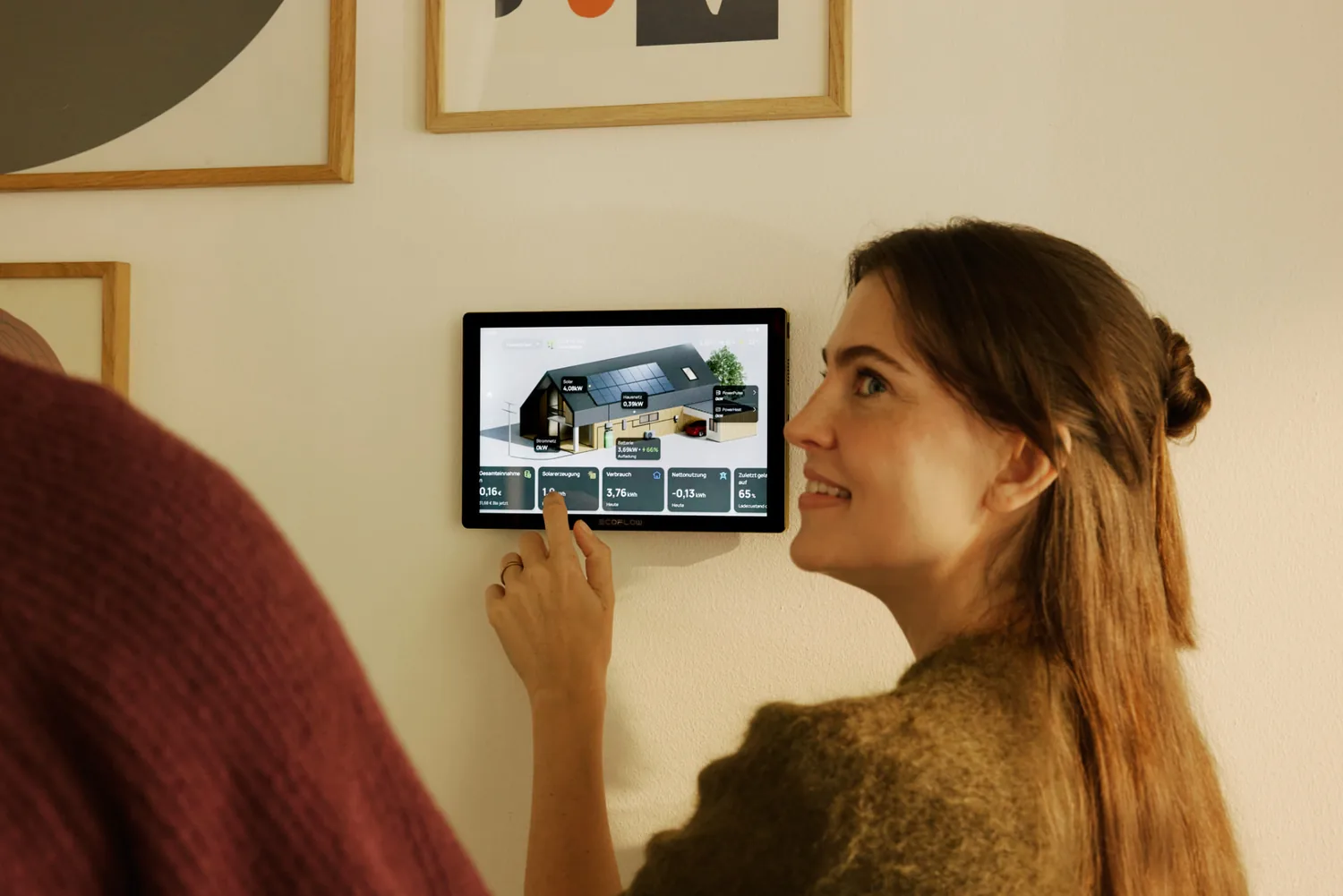 Person bedient ein wandmontiertes Touch-Display, das Erzeugung, Verbrauch und Ladezustand des Hausenergiesystems anzeigt